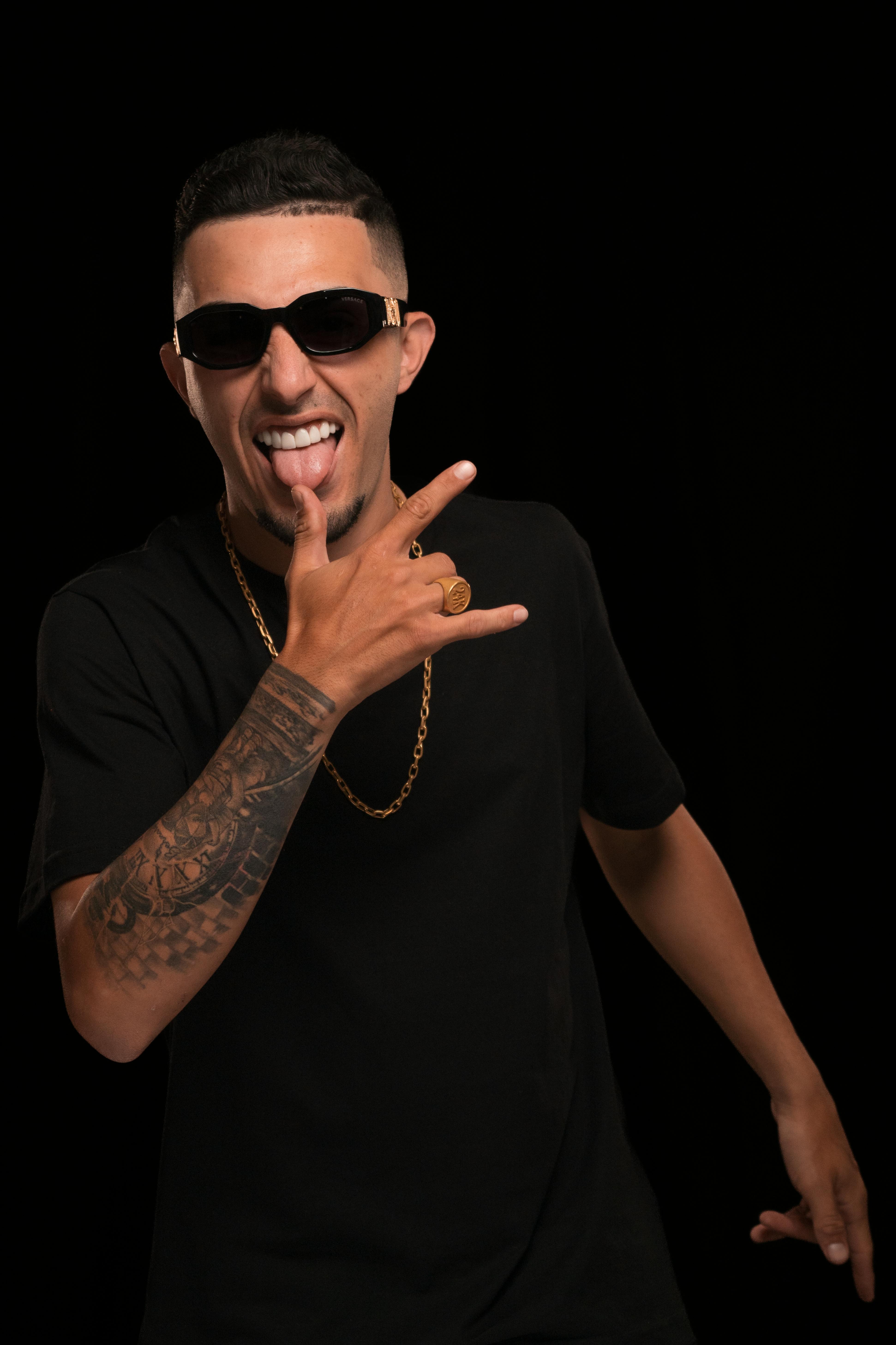 Man wearing black t-shirt and sunglasses, making a rebellious gesture against a black background.