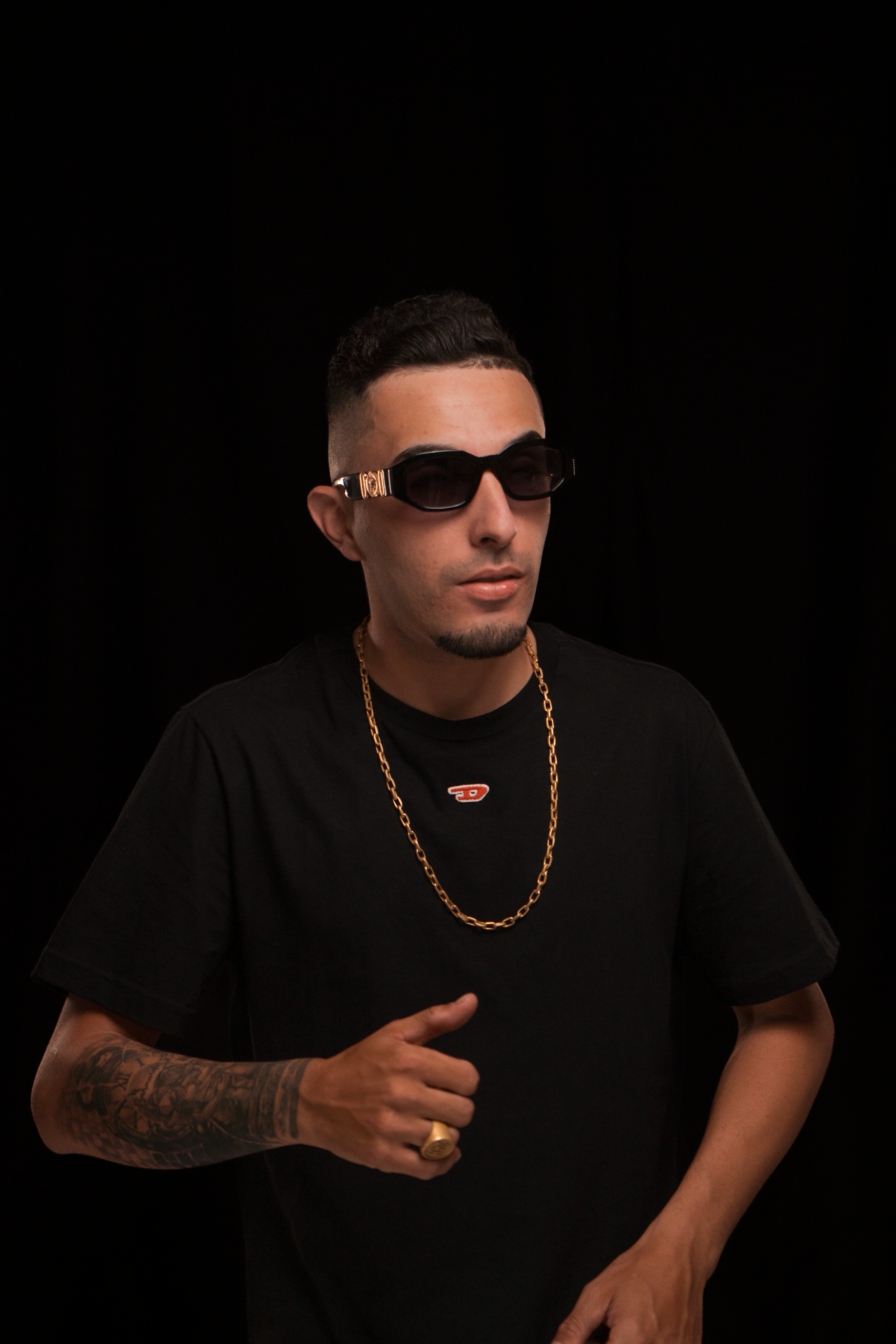 Portrait of a stylish man wearing sunglasses and a golden necklace against a black background.