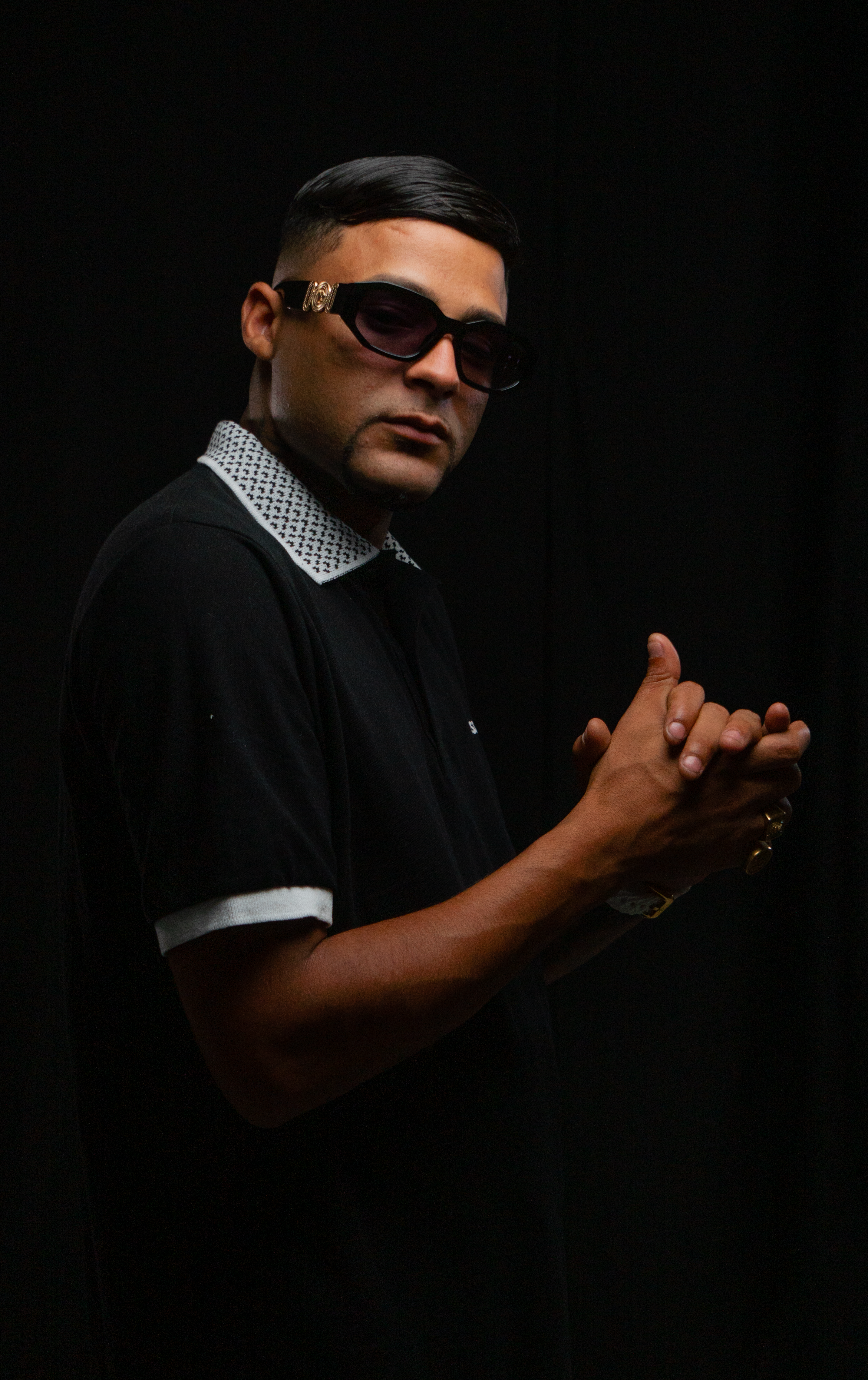 Man wearing sunglasses and black polo shirt against dark background.
