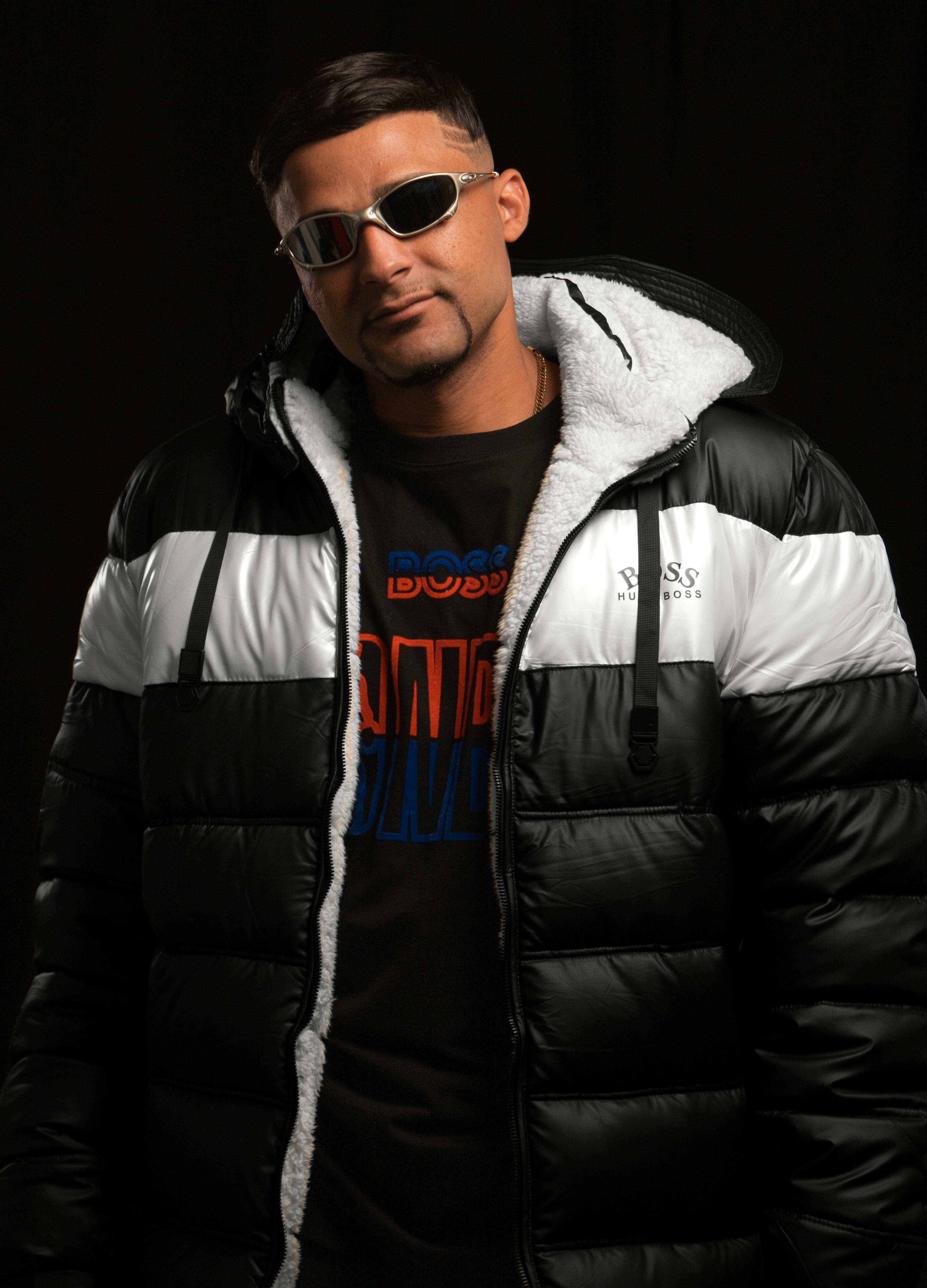 Portrait of a man wearing a puffer jacket and sunglasses against a black background.