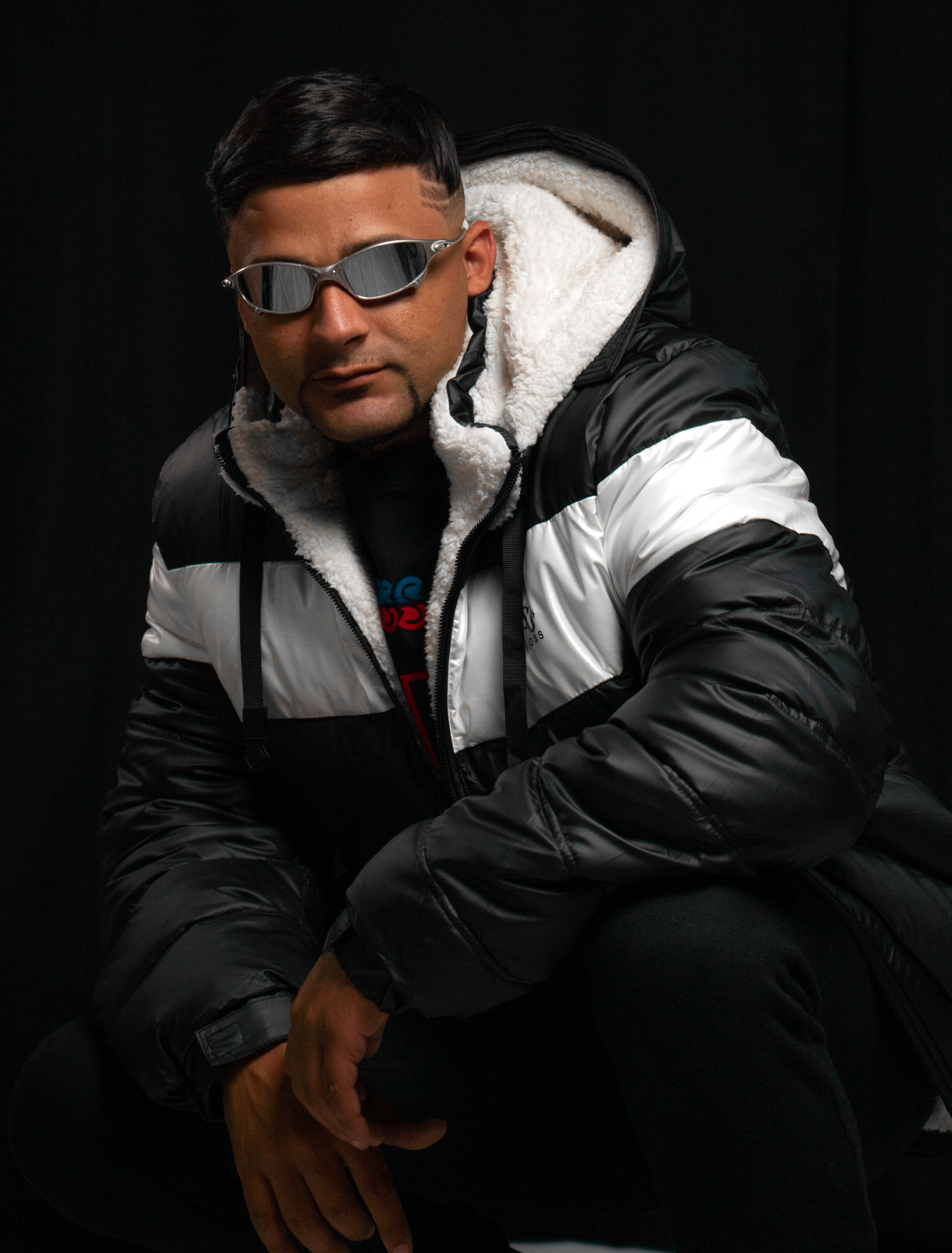 Fashionable man posing in a puffy winter jacket and sunglasses against a black background in a studio.