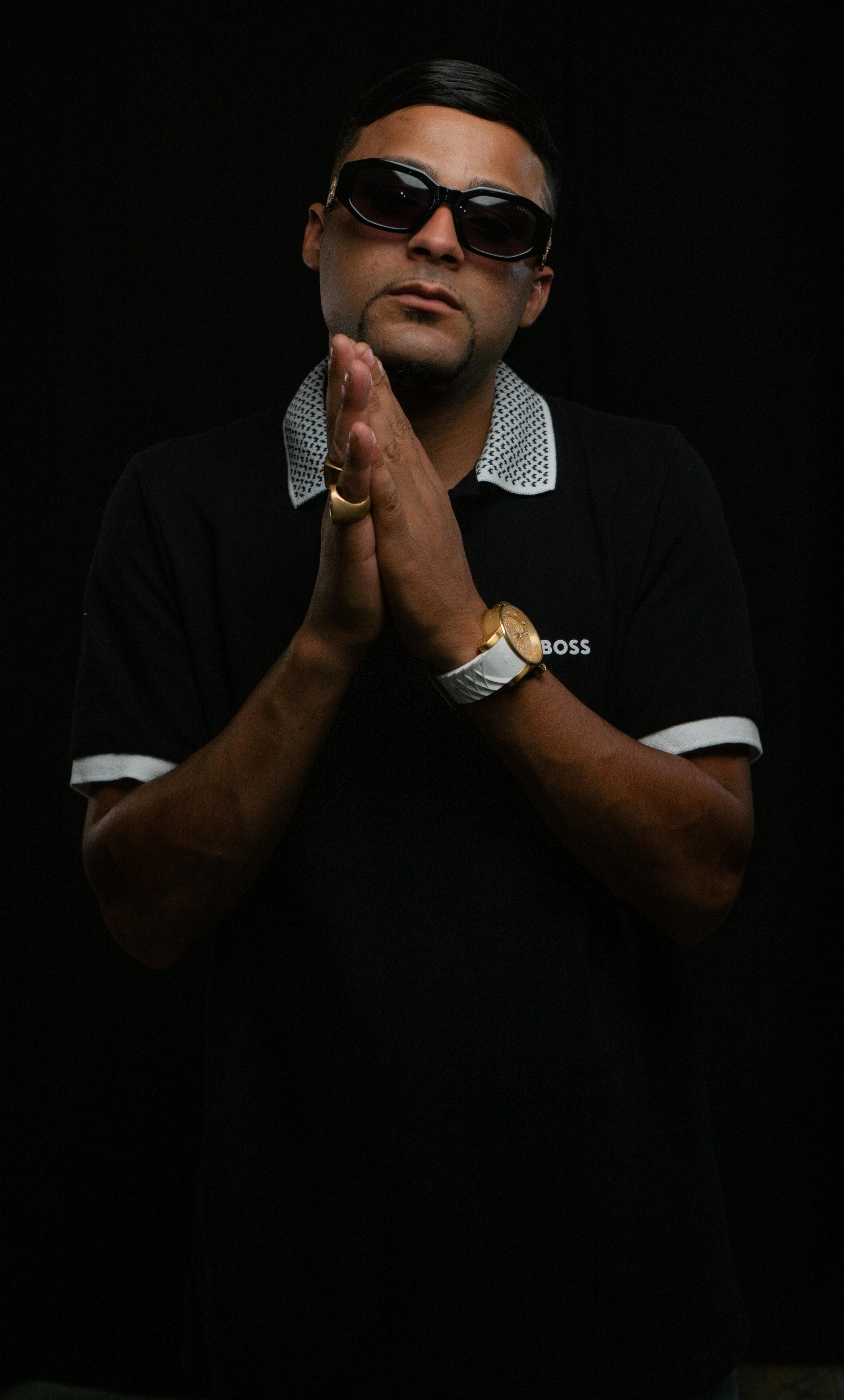 Fashionable man in sunglasses, black polo shirt, and luxury watch in a studio setting.