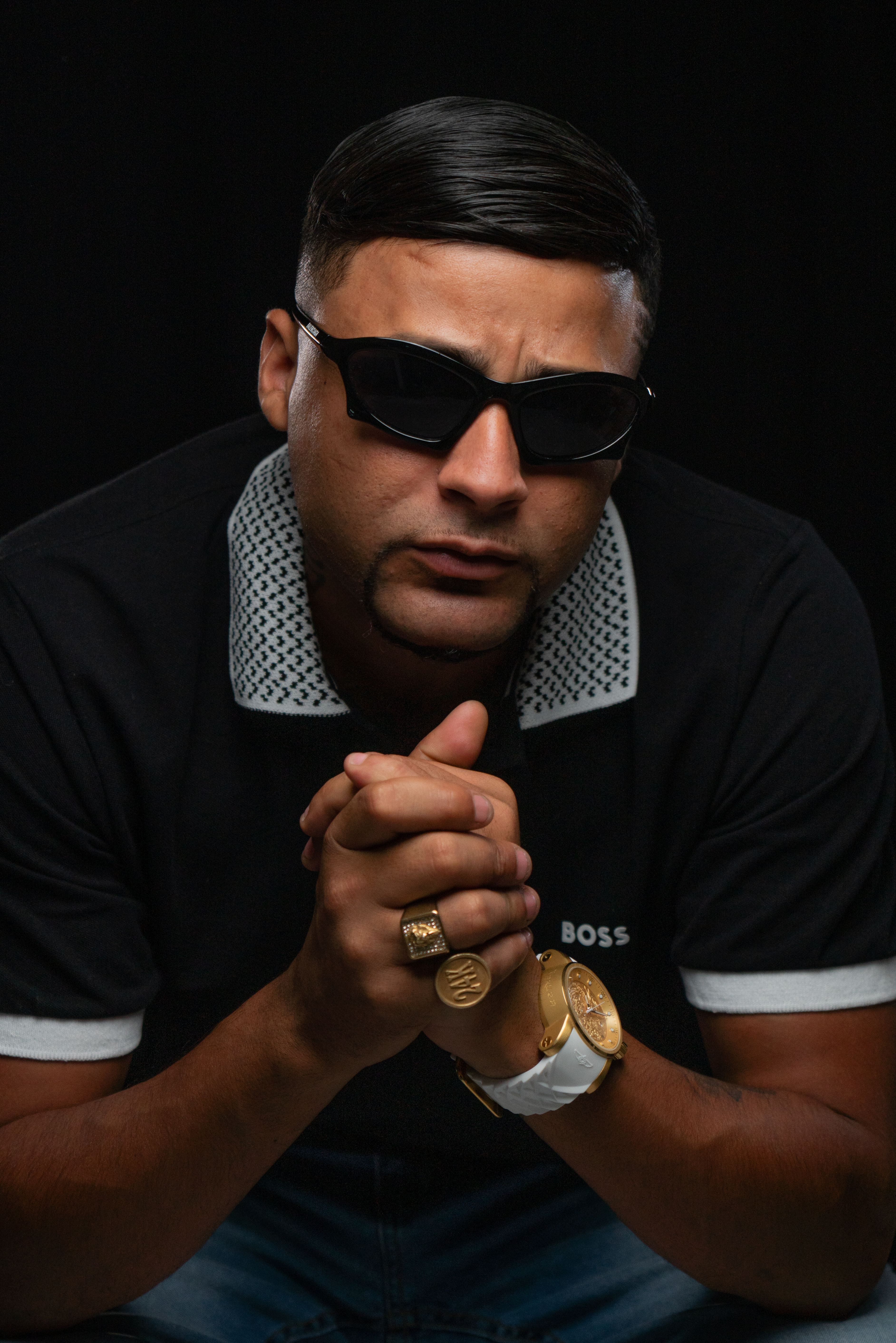 Confident man wearing sunglasses and jewelry in a dark studio pose.