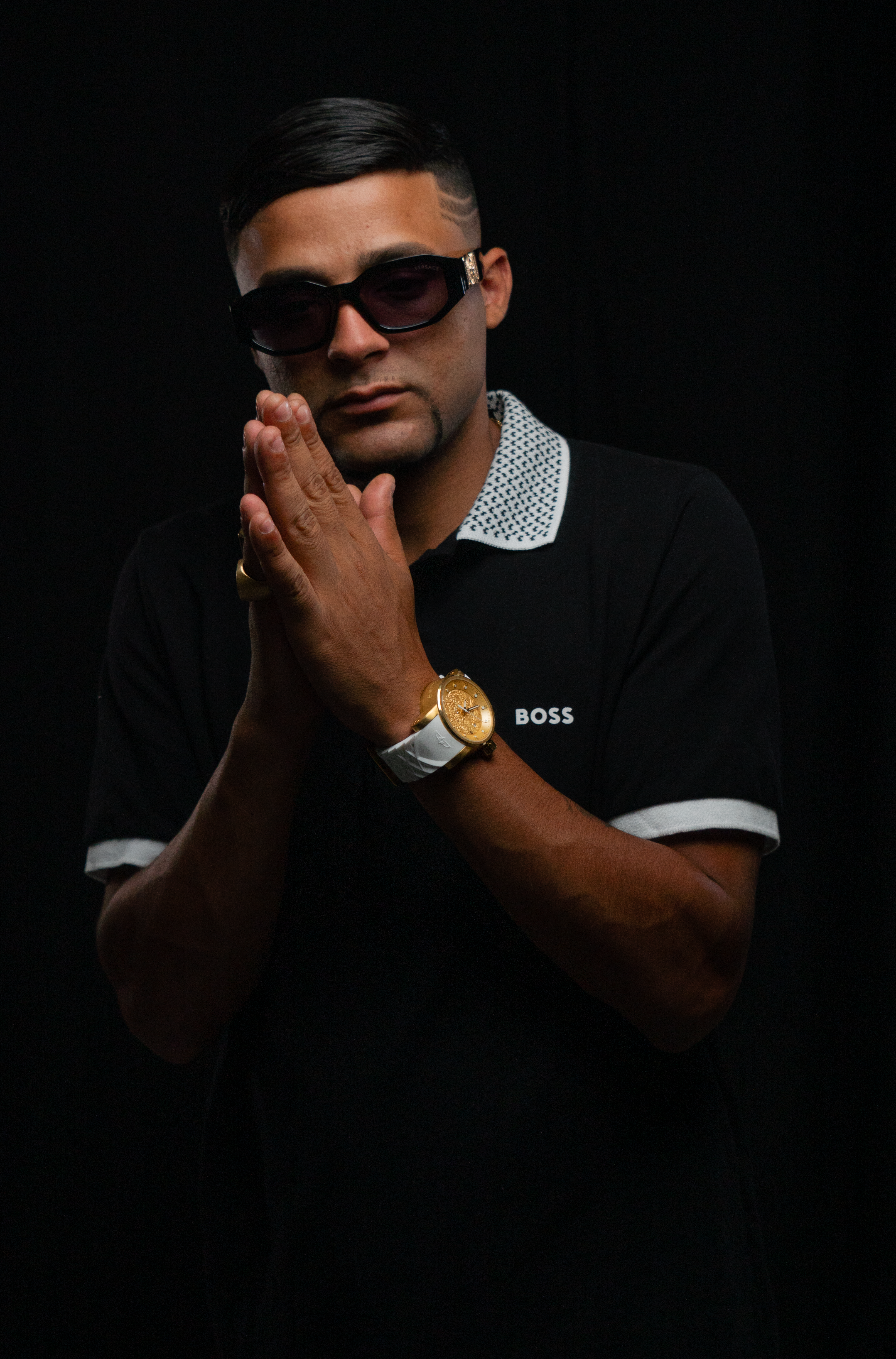 Portrait of a confident man in sunglasses and black outfit against a dark background, emphasizing style.