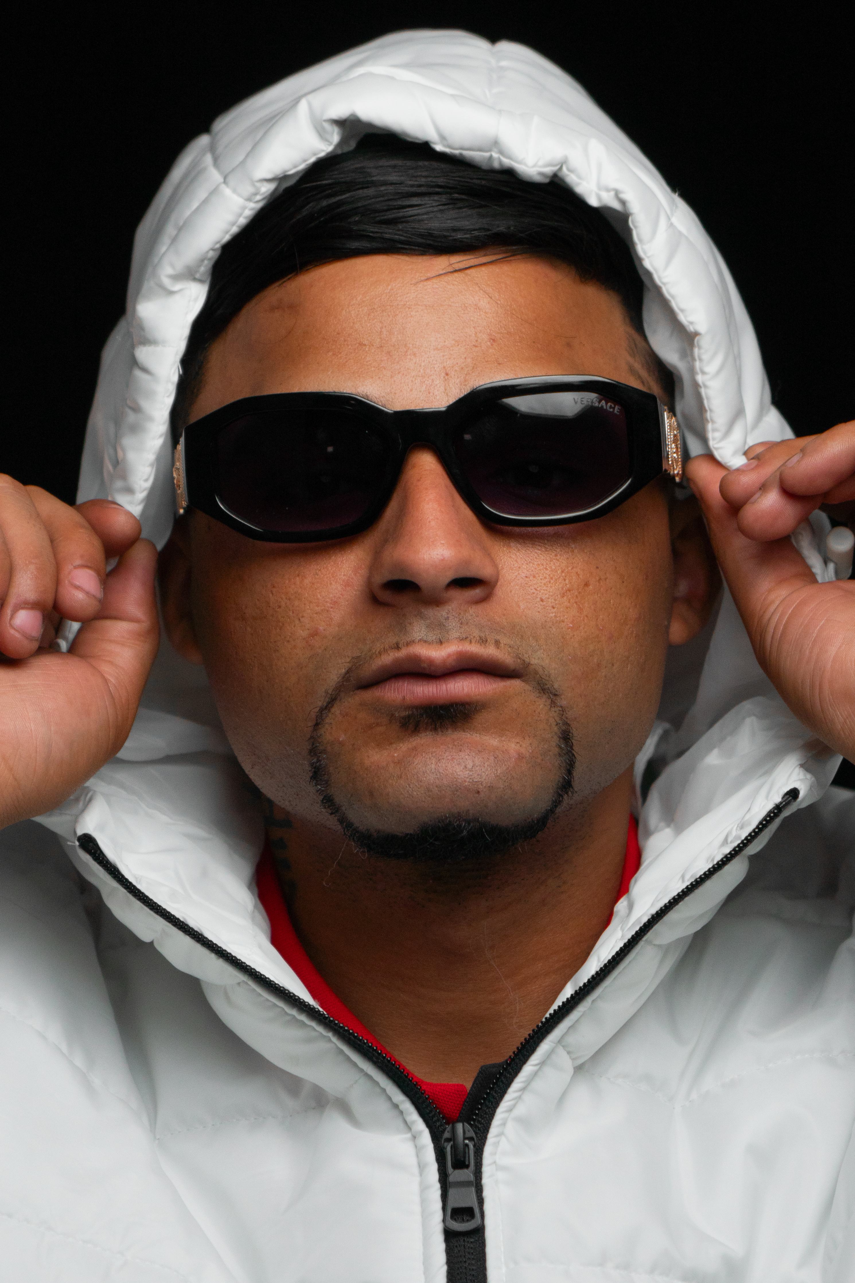 Portrait of a man adjusting sunglasses, wearing a white hoodie. Close-up shot.