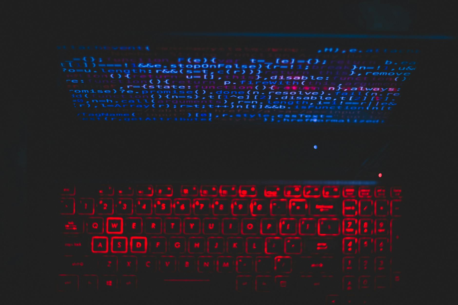 Dark-themed laptop setup with a red glowing keyboard and code on screen