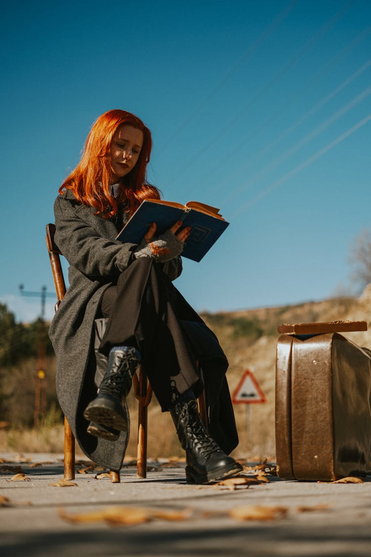 Woman Sitting On A Chair Outside And Reading A Book