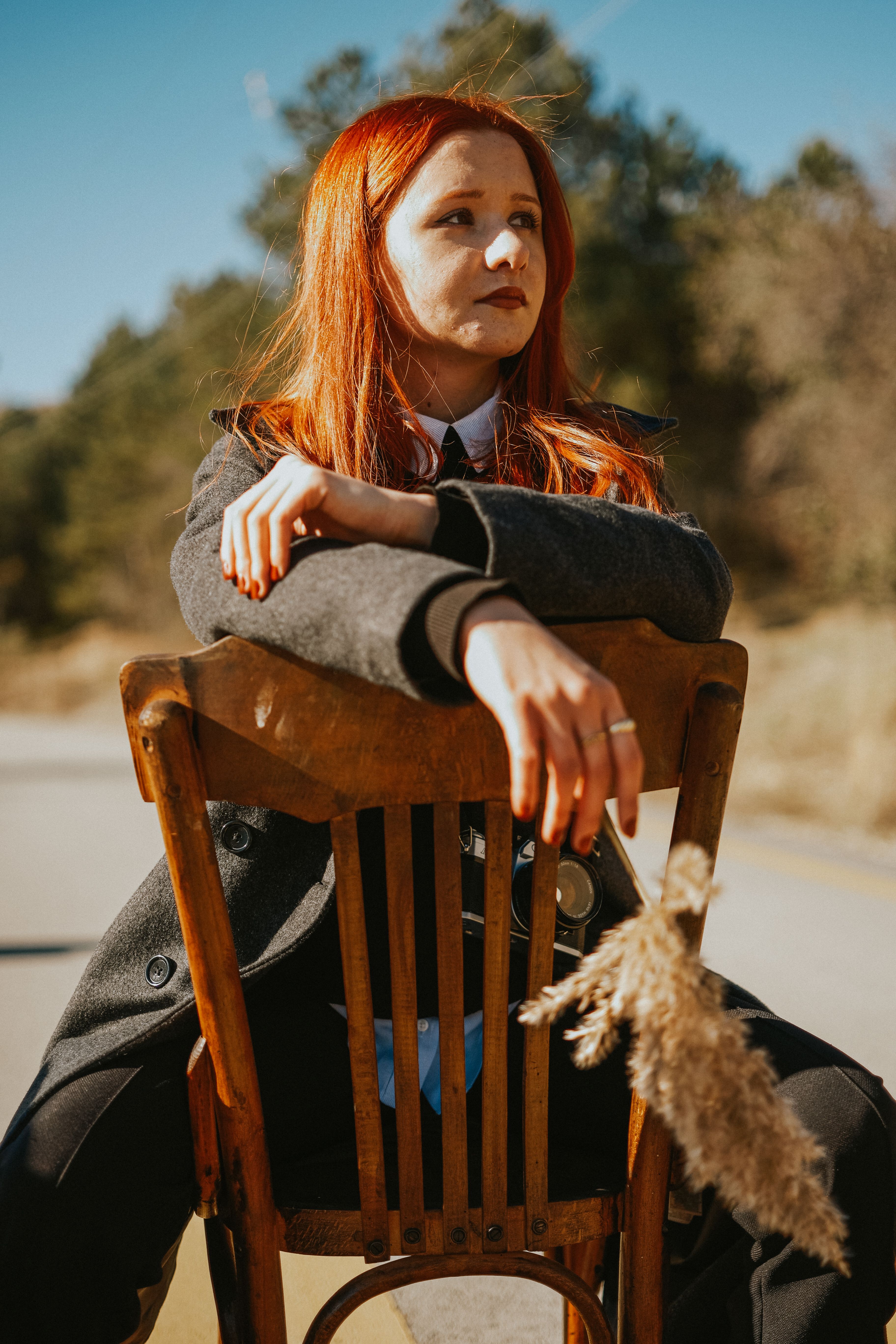 Redheaded woman in a stylish coat sitting on a wooden chair outdoors in Ankara.