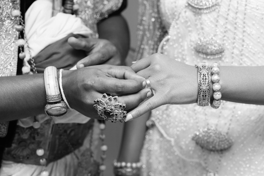 Graceful hands adorned with jewelry, exchanging rings in a black and white wedding ceremony.