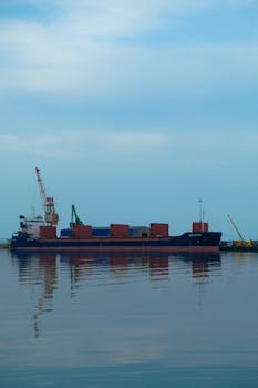 A cargo ship docked at the harbor reflecting on calm waters, showcasing maritime transportation.