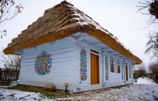 A traditional thatched cottage with colorful murals set against a snowy backdrop, exemplifying rustic charm.