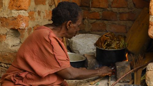Free An elderly African woman cooks traditional food over an open fire in a rustic kitchen. Stock Photo