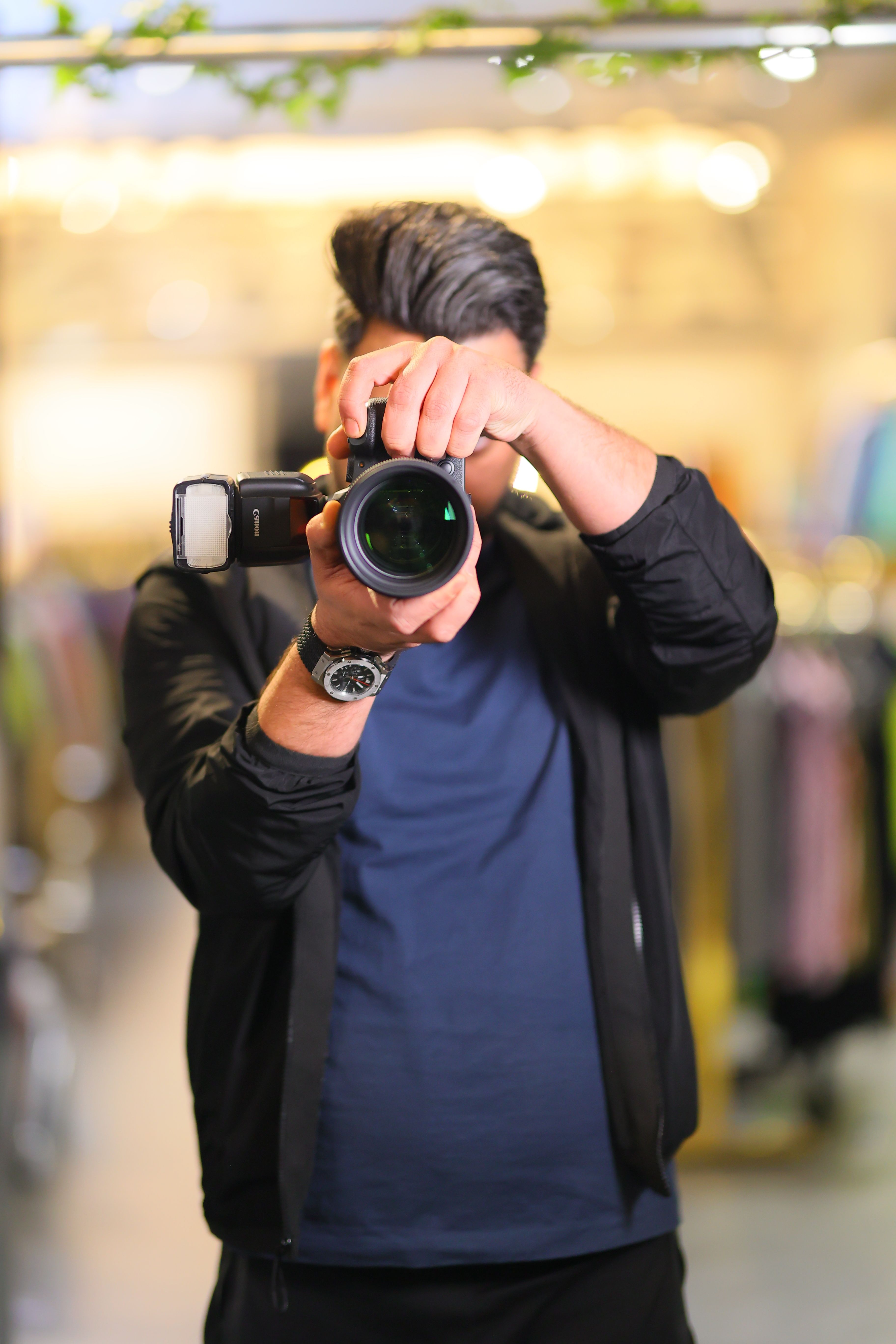 Man taking a photo indoors with a camera, wearing a jacket and watch.
