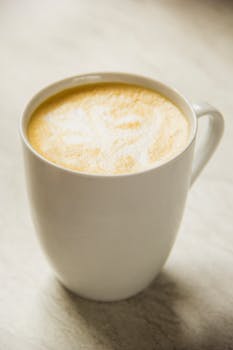 A close-up of a creamy latte with intricate art in a white mug on a marble table.