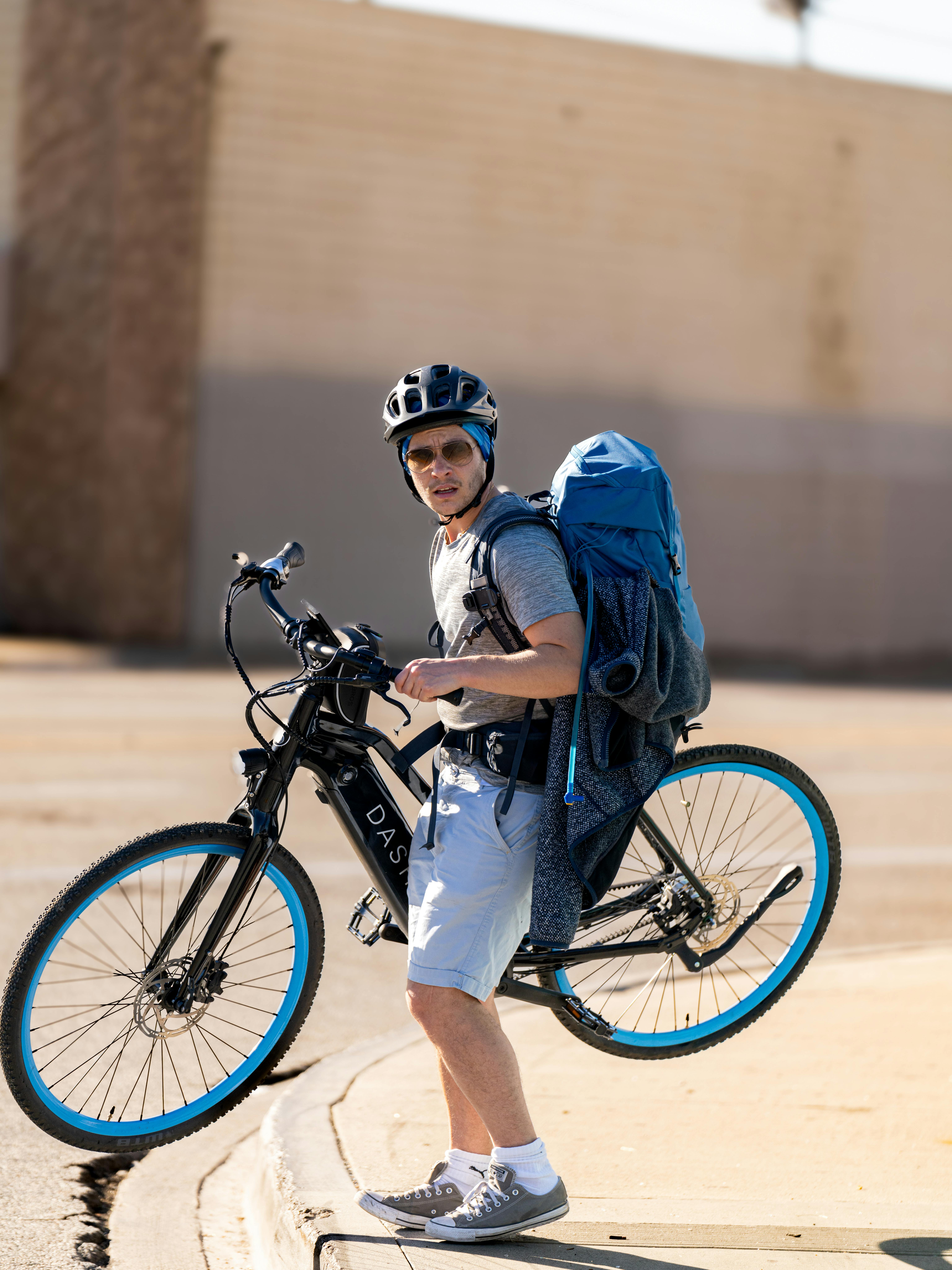 Man riding bicycle wearing backpack and helmet in urban environment on a sunny day.