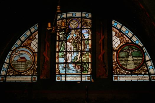 Intricate stained glass window portraying a biblical baptism scene in a church setting.
