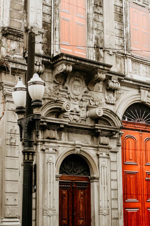 Free Detailed view of an ornate historical building facade featuring red doors, carved stone, and vintage architecture. Stock Photo