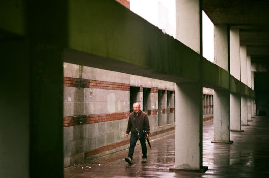A man walks through a wet concrete passageway in an urban setting during a rainy day.