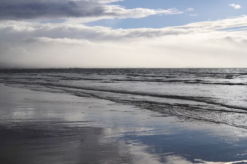 Free Peaceful beach scene with gentle waves and dramatic clouds along the coastline. Stock Photo