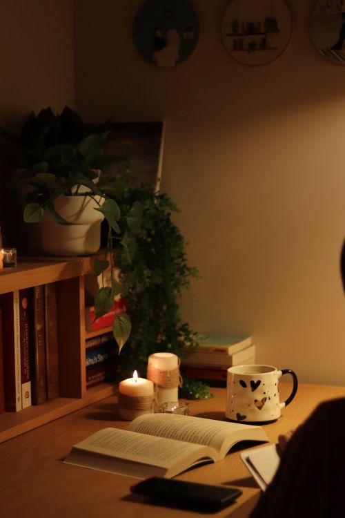 Free Warm and inviting home desk setup with books, candles, and a cup, perfect for relaxation and reading. Stock Photo
