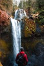 一个穿着红色夹克的男人，在充满活力的森林景观中，敬畏地望着瀑布