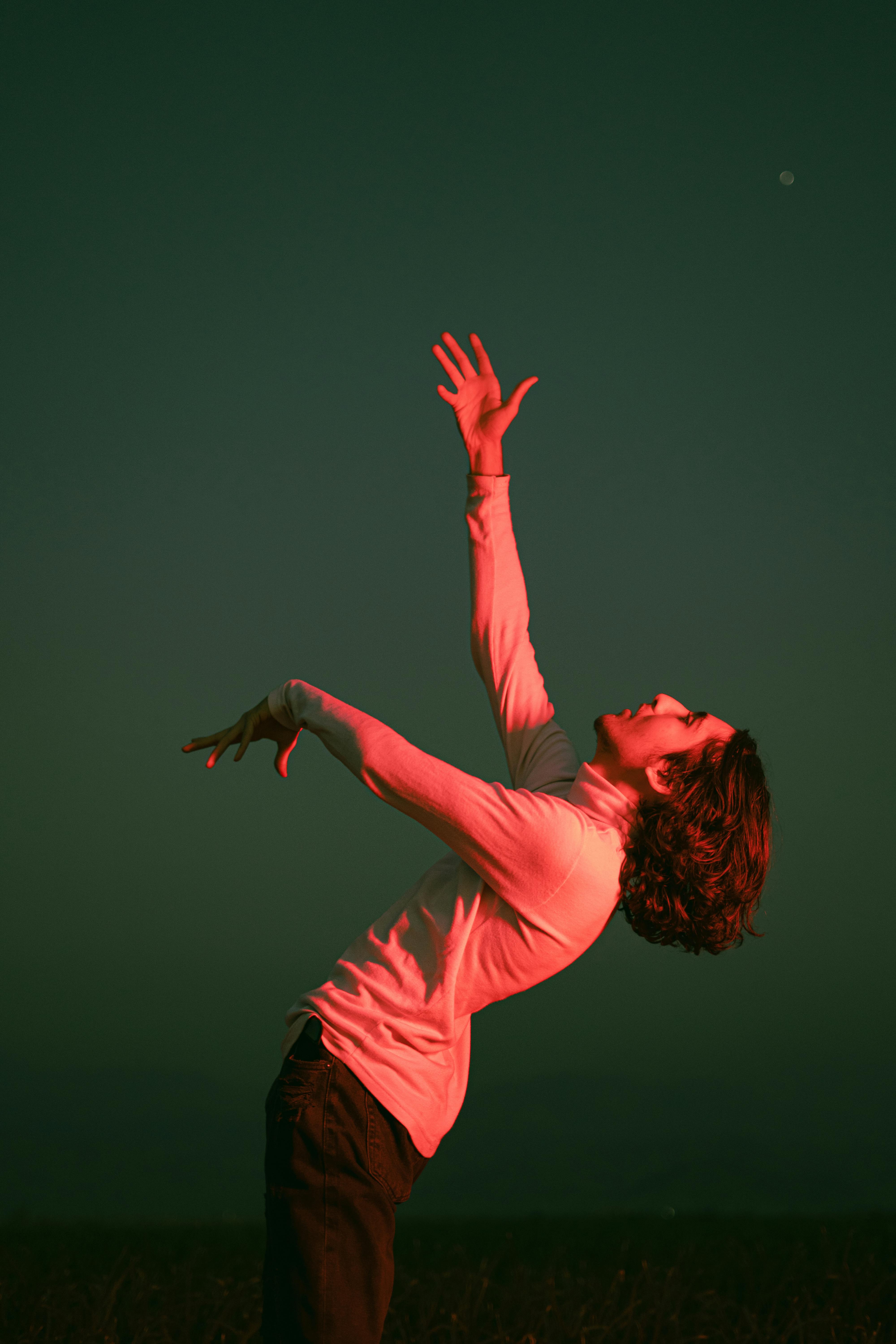 Young man with arms raised in dramatic pose under colorful night sky in Jiroft, Iran.