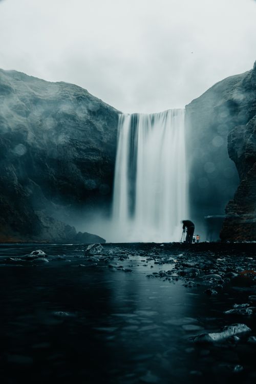Free A dramatic waterfall cascades between rugged cliffs, surrounded by mist and serene natural beauty. Stock Photo