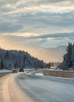 Snowy road surrounded by trees and mountains during winter in Banff, Alberta.