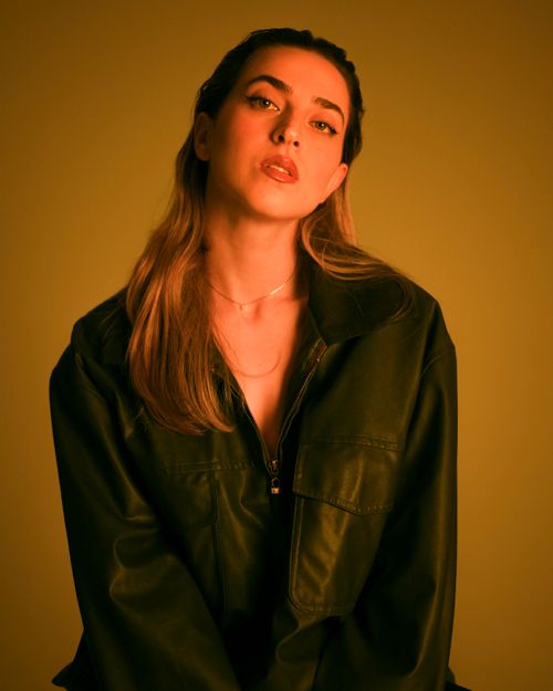 Free Stylish woman in a leather jacket posing against a warm yellow background. Stock Photo