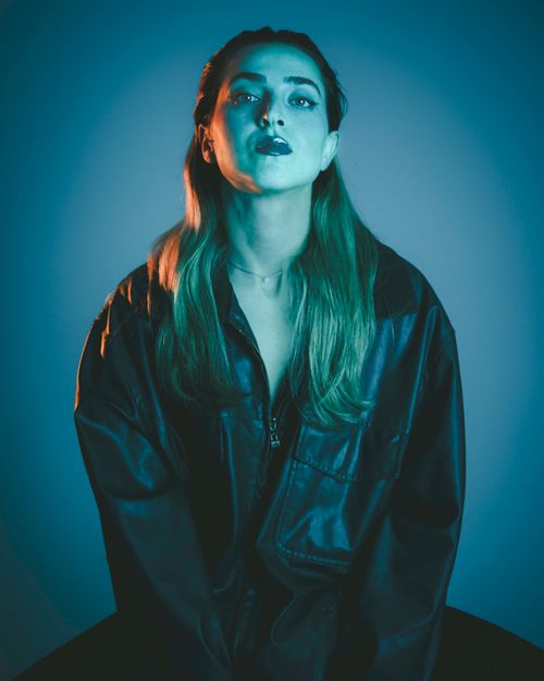 Free Stylish portrait of a woman wearing a leather jacket in a studio setting with blue lighting. Stock Photo