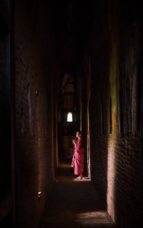 Free A monk in a pink robe praying in a narrow, dark corridor with light from above. Stock Photo