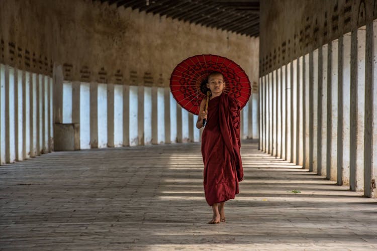 Boy In Red Robes Walking With Umbrella