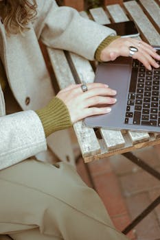 Close-up of a woman's hands typing on a laptop outdoors, showcasing fashion and technology.