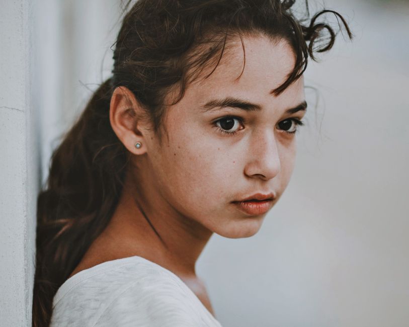 Retrato en primer plano de una joven pensativa con cabello rizado castaño frente a un fondo neutral.