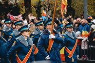 A military parade in Bucharest featuring uniformed soldiers marching with flags amidst a gathered crowd.