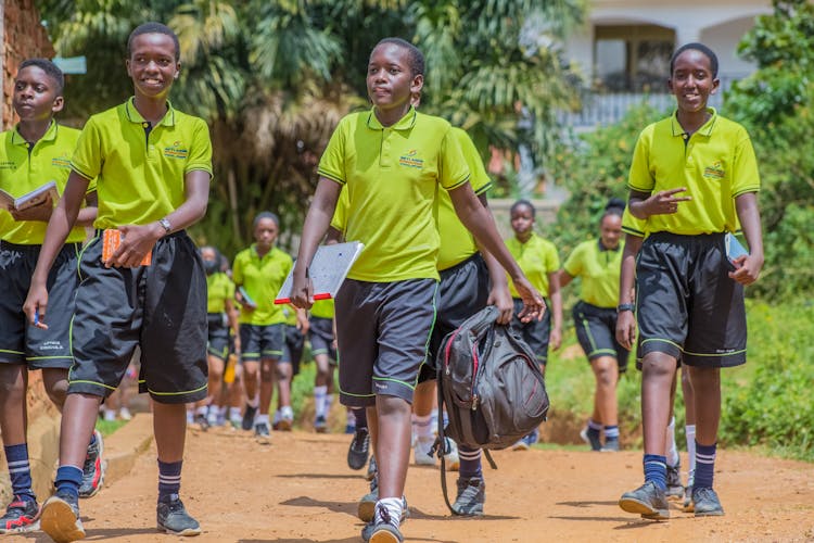 Students In School Uniforms Walking Along A Gravel Road