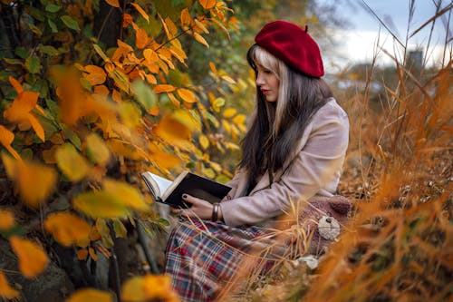 A Woman Sitting on a Field in Autumn and Reading a Book 