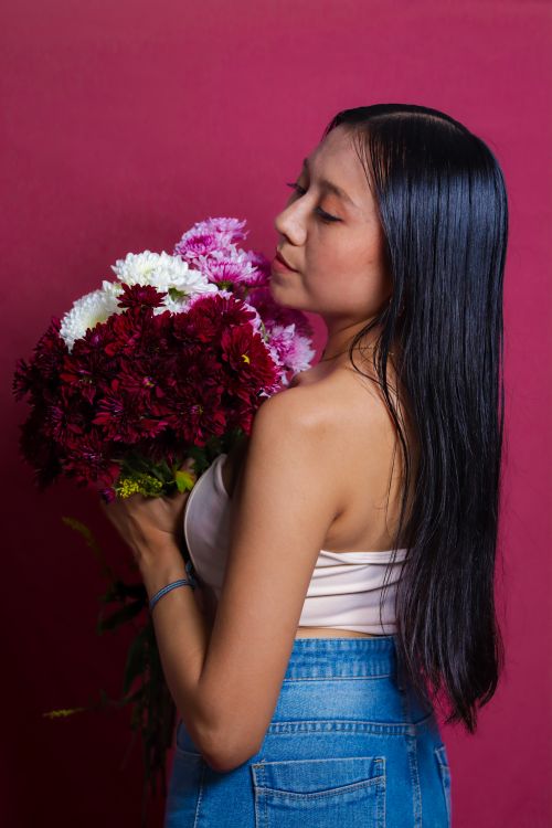 Free A serene portrait of a woman holding a vibrant bouquet against a red background, exuding elegance and grace. Stock Photo