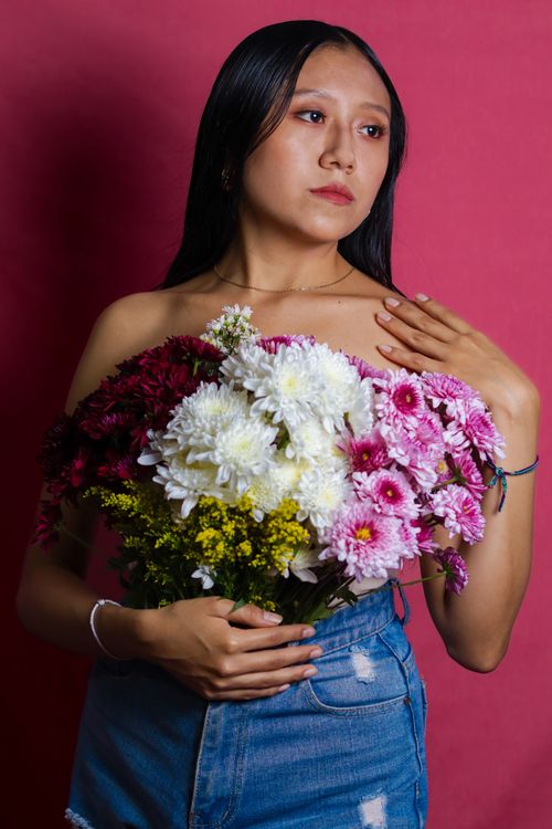 Free A woman in jeans holding a vibrant floral bouquet against a pink backdrop. Stock Photo