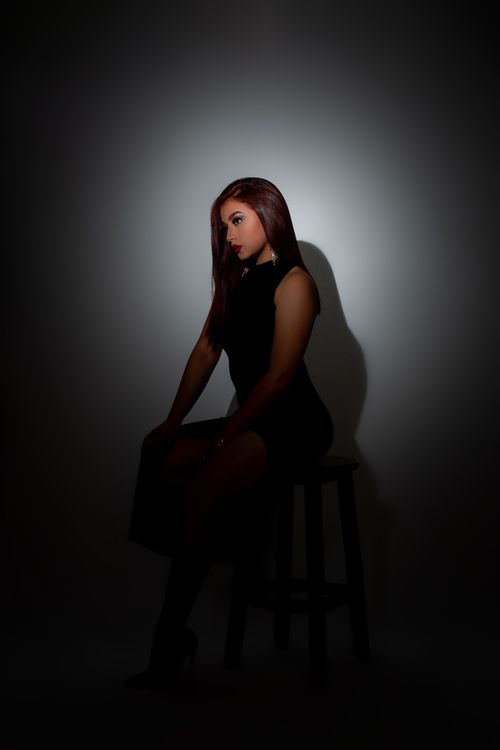 Free Striking low-light portrait of a stylish woman seated, showcasing elegance and mystery. Stock Photo