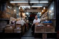 An elderly man sitting in an Asian dry goods store filled with boxes and bags at night.