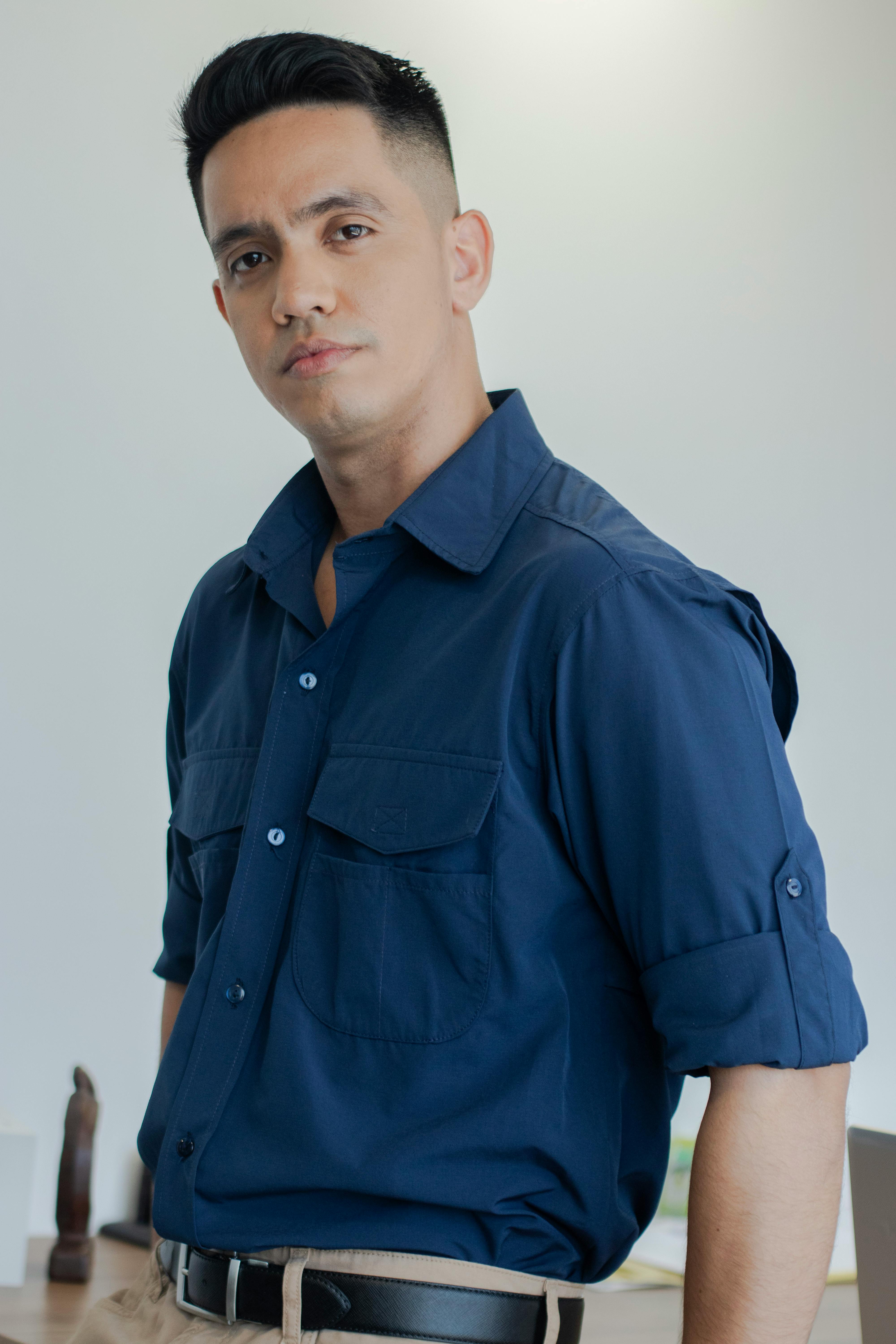Confident man in a blue shirt posing indoors with a serious expression.