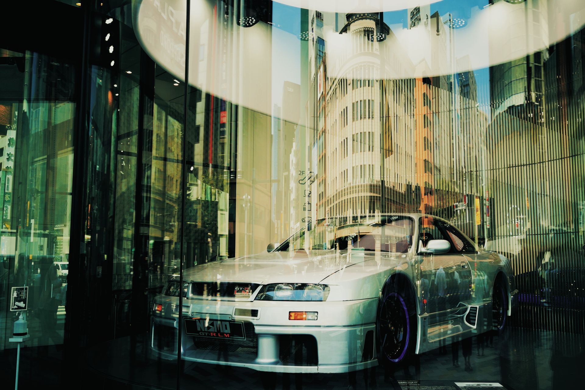 A sleek silver car showcased in a modern city display window with urban reflections.