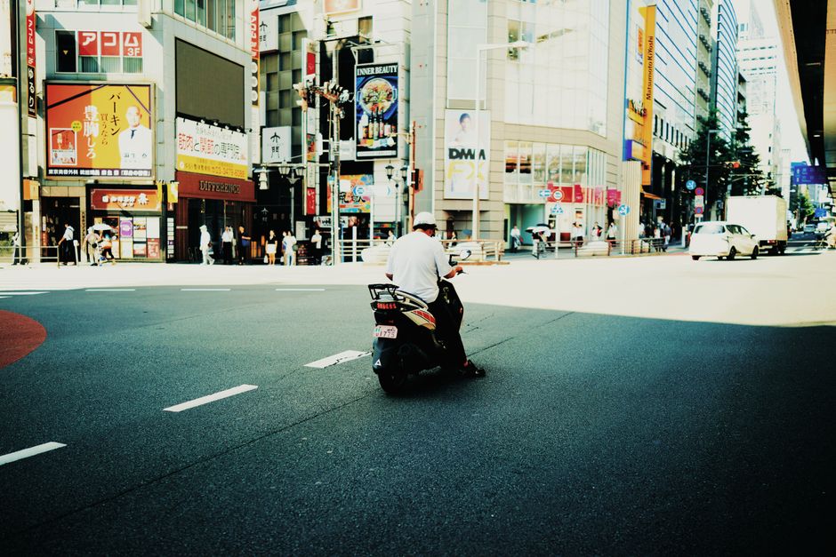 A man riding a motor scooter in a vibrant urban cityscape, surrounded by tall buildings.