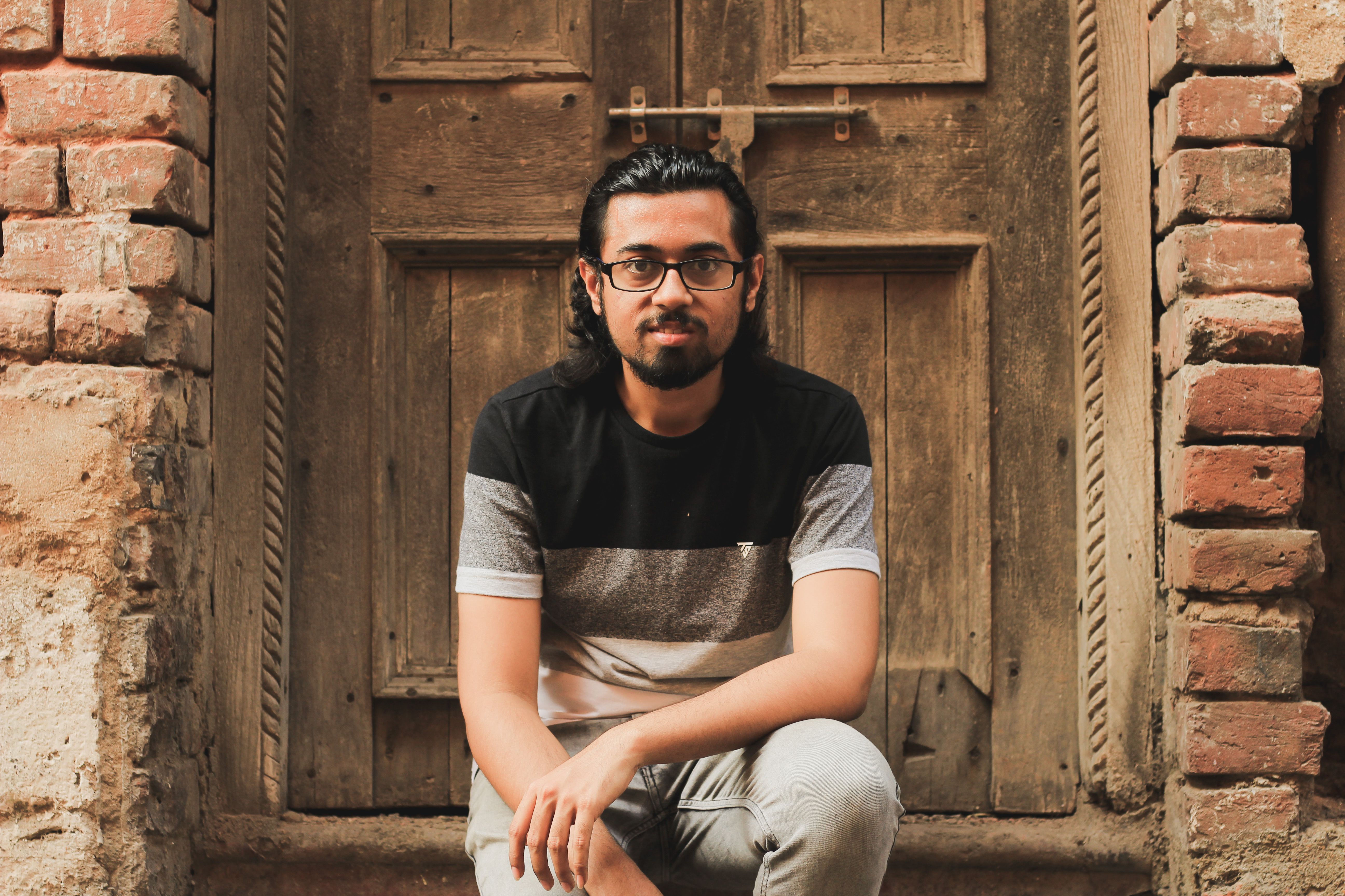 Man in casual attire sitting against an old wooden door, exuding a relaxed vibe.