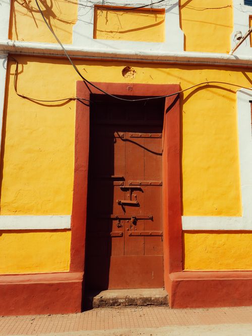 Free A vibrant yellow facade featuring a rustic wooden door with red trim in sunlight. Stock Photo
