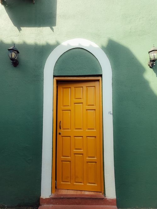 Free A colorful yellow door set in a green wall with a classic arch design and lamps. Stock Photo