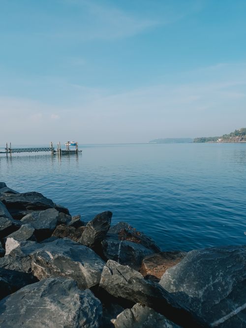 Free Serene seascape featuring rocks and a pier extending into the blue sea under clear skies. Stock Photo