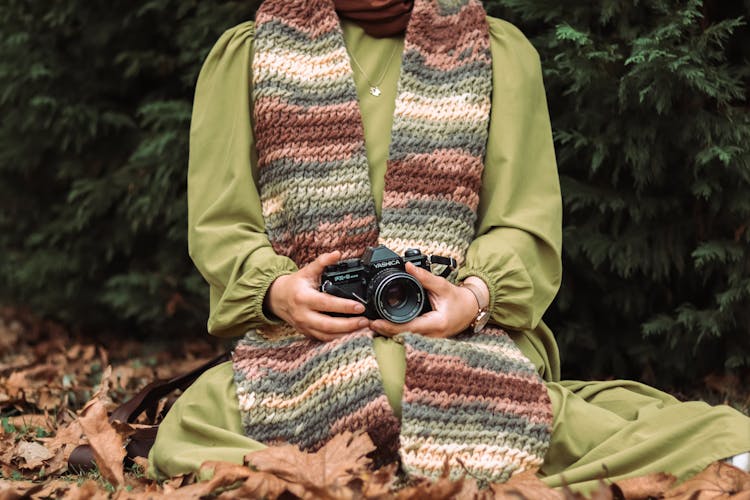 Person With Scarf In Green Coat Sitting With Camera In Hands