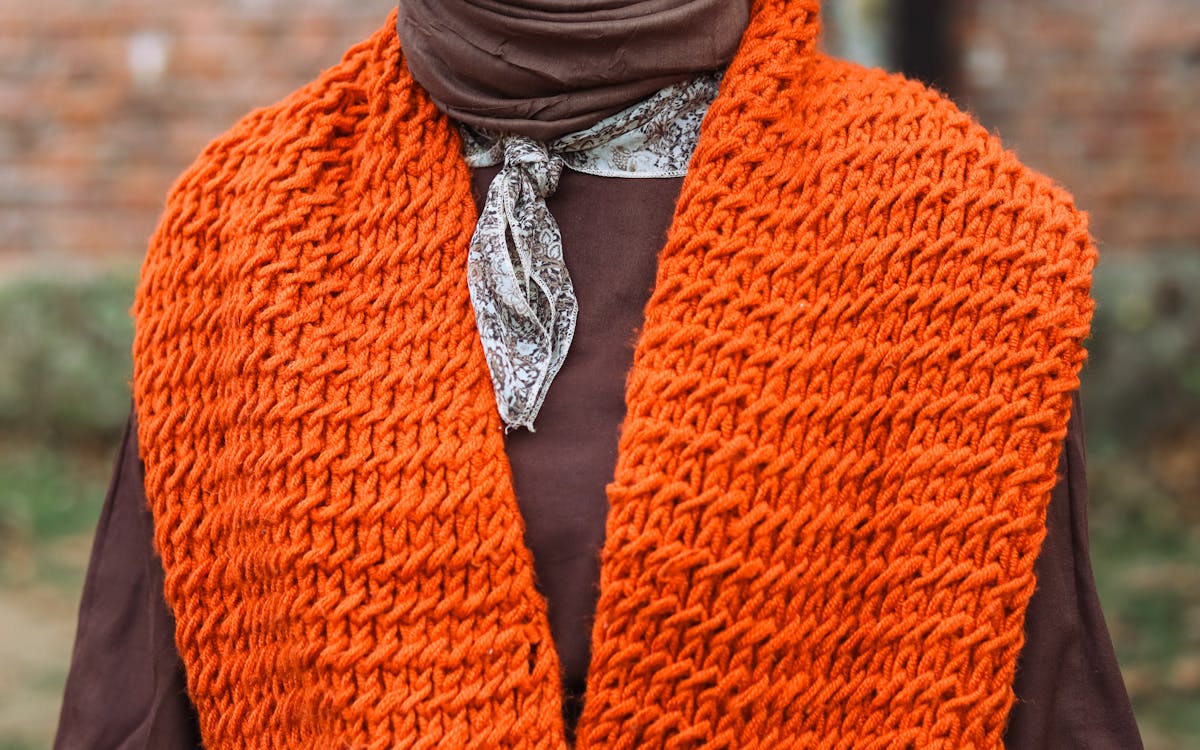 Close-up of a stylish orange knit scarf and brown outfit, perfect for fall fashion enthusiasts.